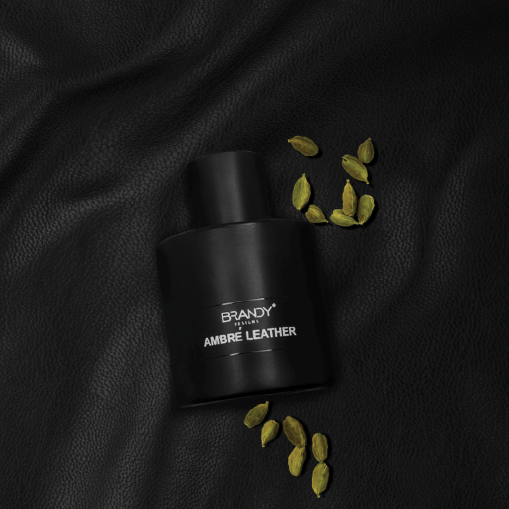 Black perfume bottle labeled 'Brandy' with cardamom pods on a black leather background