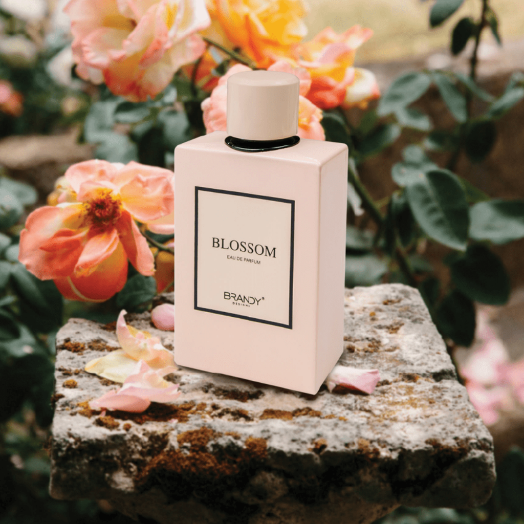 Perfume bottle labeled 'Blossom' by Brandy on a stone surface with flowers in the background
