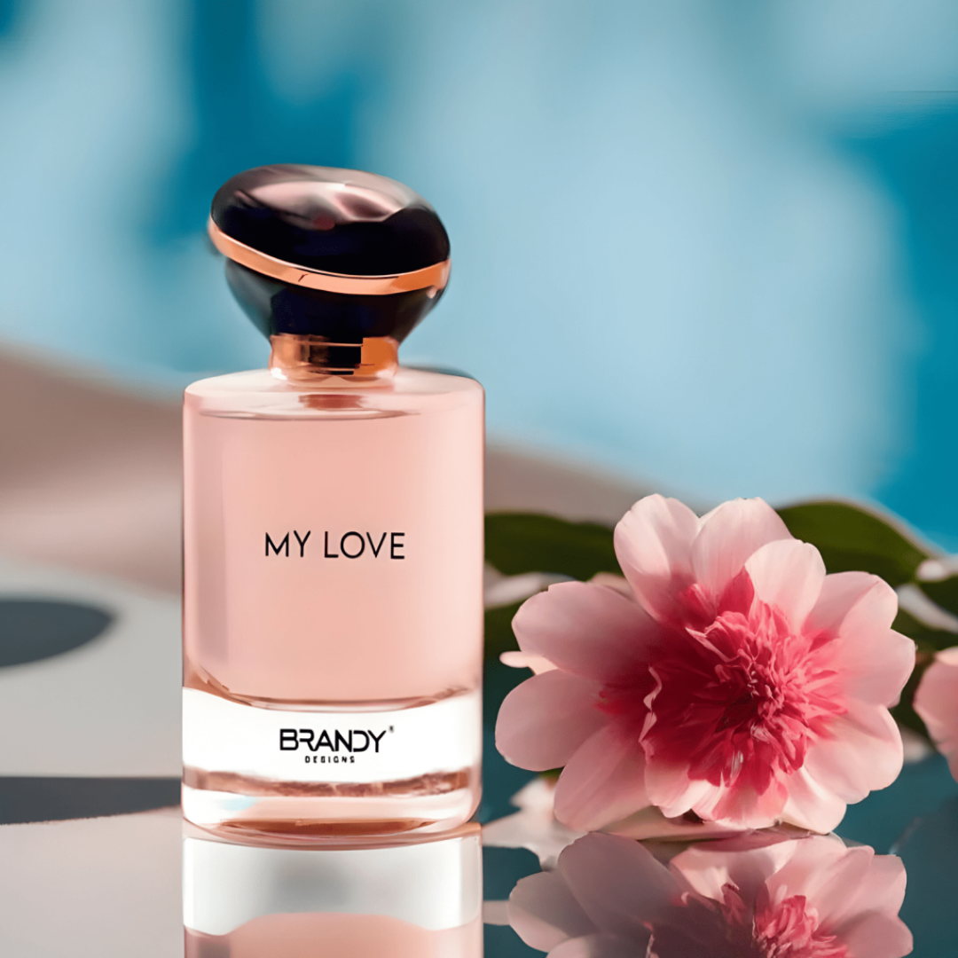 Perfume bottle labeled 'My Love' by Brandy with a pink flower on a reflective surface.
